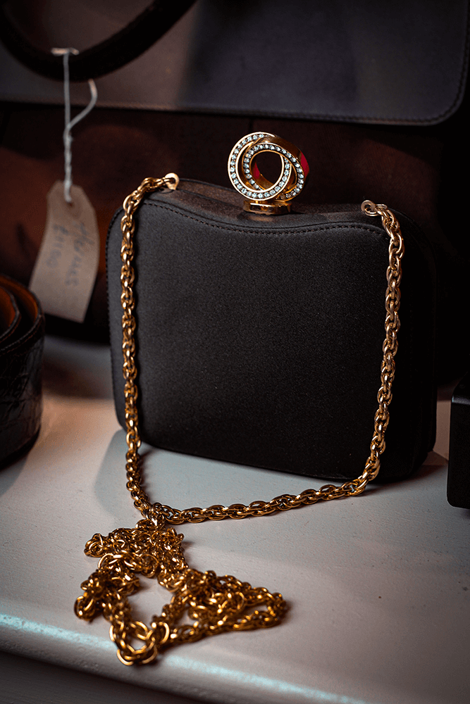 A Constantine Rex black and gold vintage clutch sitting on a wooden shelf in a romantic boutique.