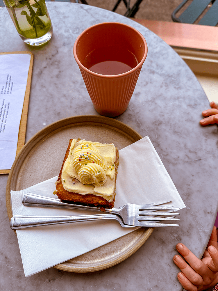 A slice of 'Birthday cake' with butter cream and sprinkles on a marble café table.
